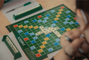 Students engaged in game-based learning with educational games like Scrabble and Guess Who in a classroom.