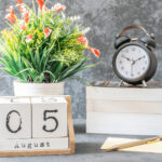 August calendar with flowers on the table with a book and clock.