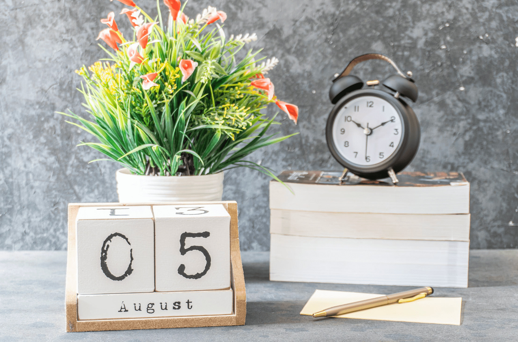 August calendar with flowers on the table with a book and clock.